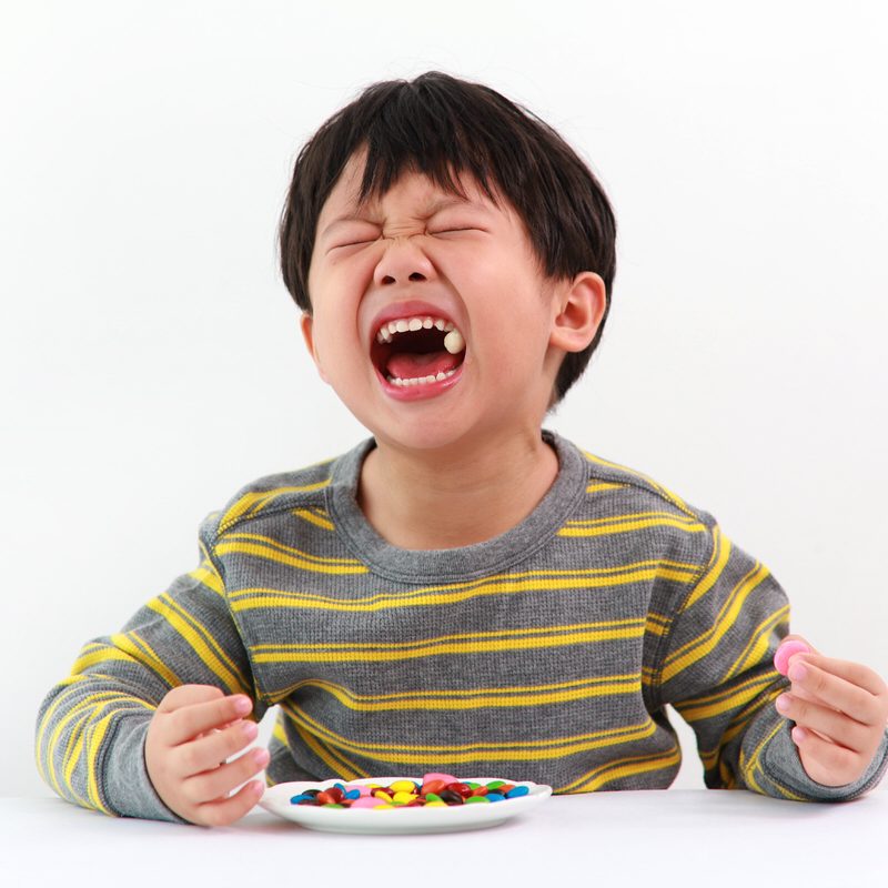 Asian boy with toothache Sad little Asian boy suffering from toothache pain in mouth while eating candy.